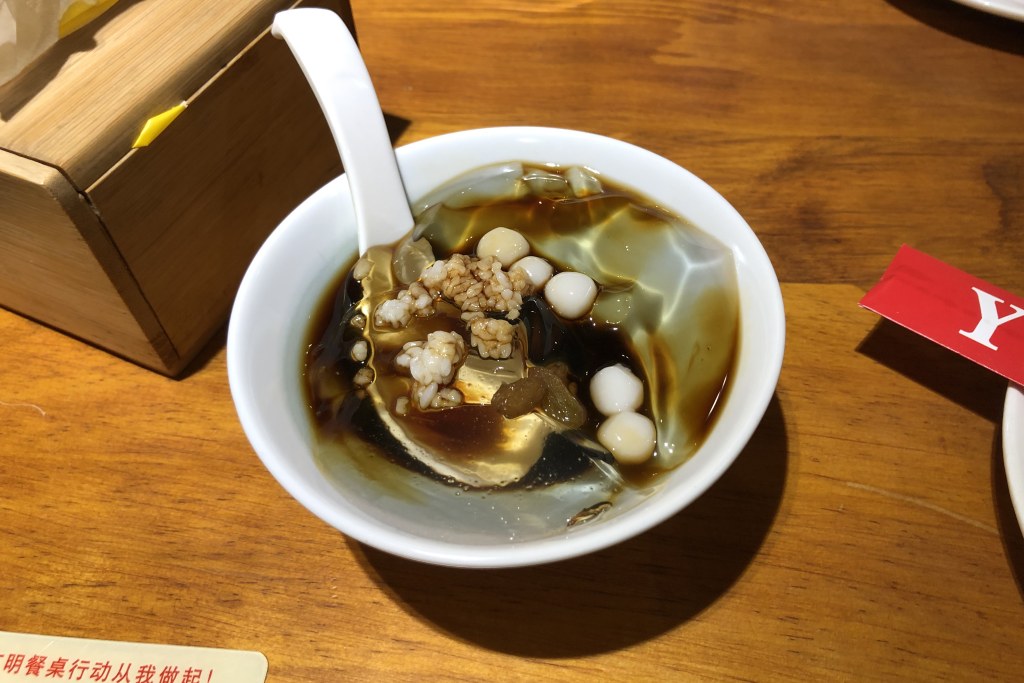 A bowl of Sichuan bingfen ice jelly in brown sugar syrup topped with peanuts and fermented rice